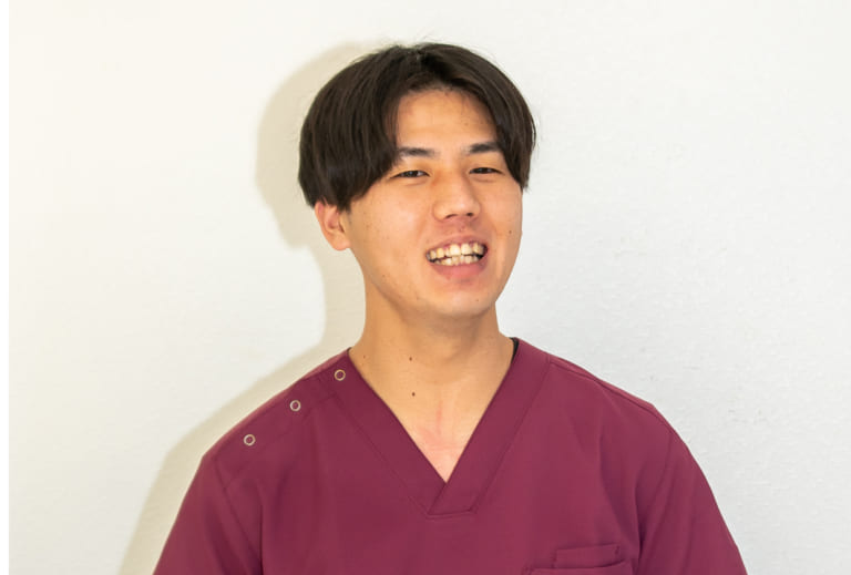 鍼灸師の朝倉さんがマルーン色の制服で笑顔を見せている写真