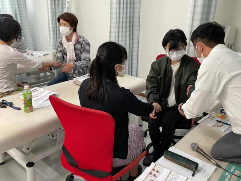 マスクを着けたスタッフが利用者の手を握って説明している診療室の場面