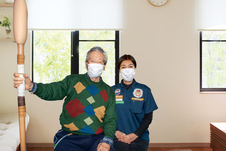 豊橋の自宅で腰痛治療を受ける高齢男性と訪問リハビリマッサージを行う女性スタッフ
