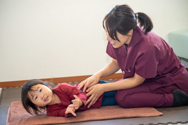 母親が子どもを介助し、リハビリマッサージを行っている場面
