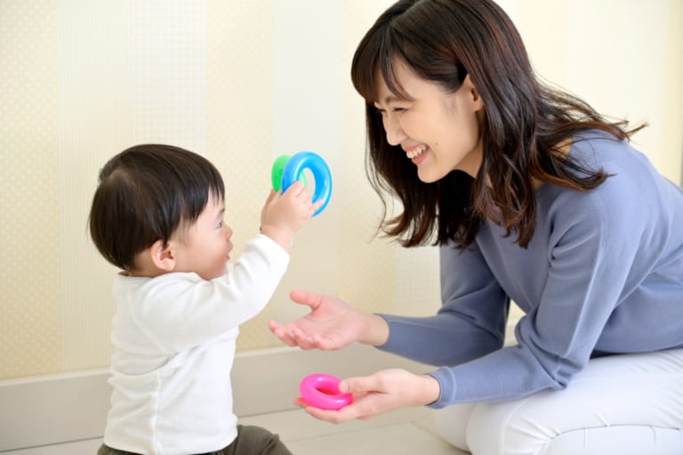 笑顔の女性が赤ちゃんにおもちゃのリングを手渡して遊ぶ場面