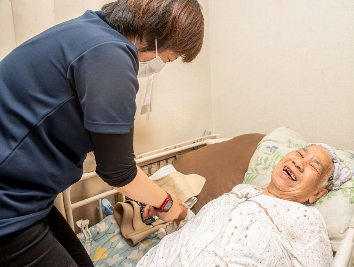訪問マッサージを受ける高齢女性を介護者がベッドでケアしている様子